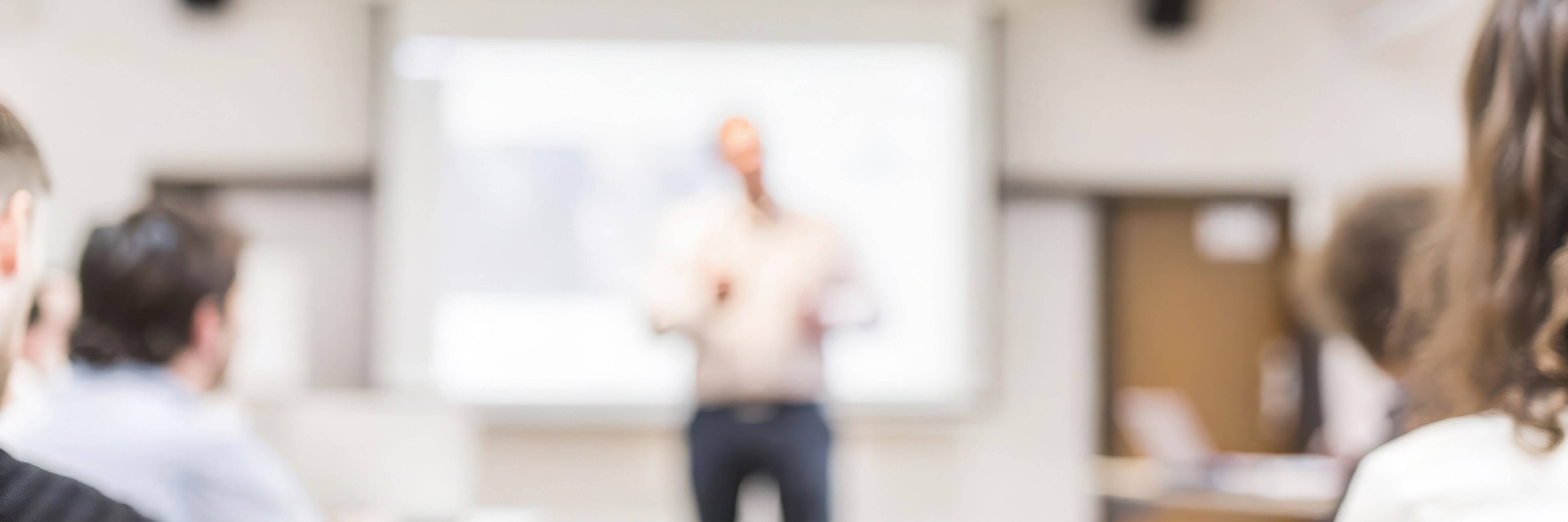 A blury image of a meeting room with someone infront of a whiteboard.