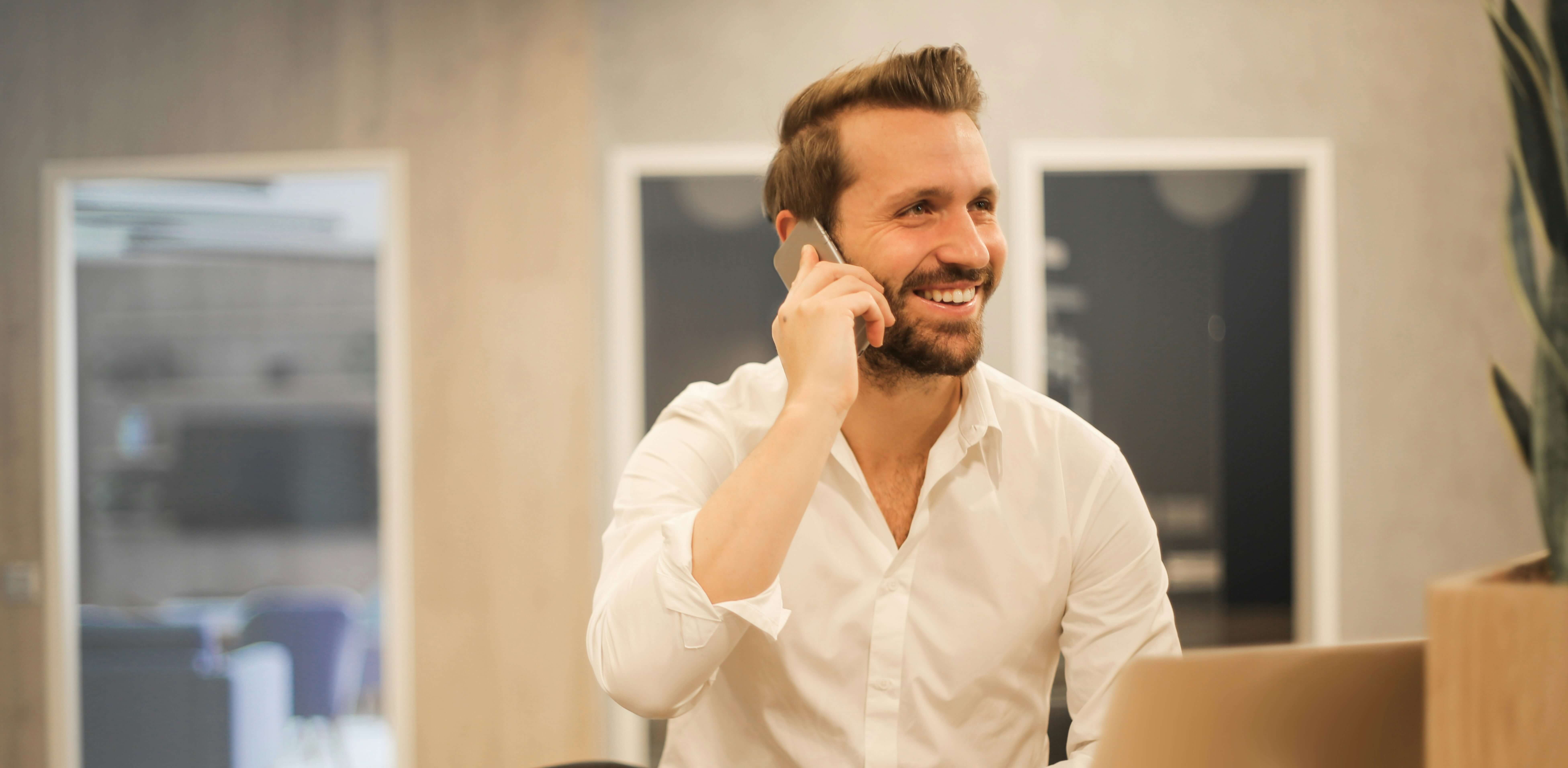 A man smiling holding a phone in a modern office space.