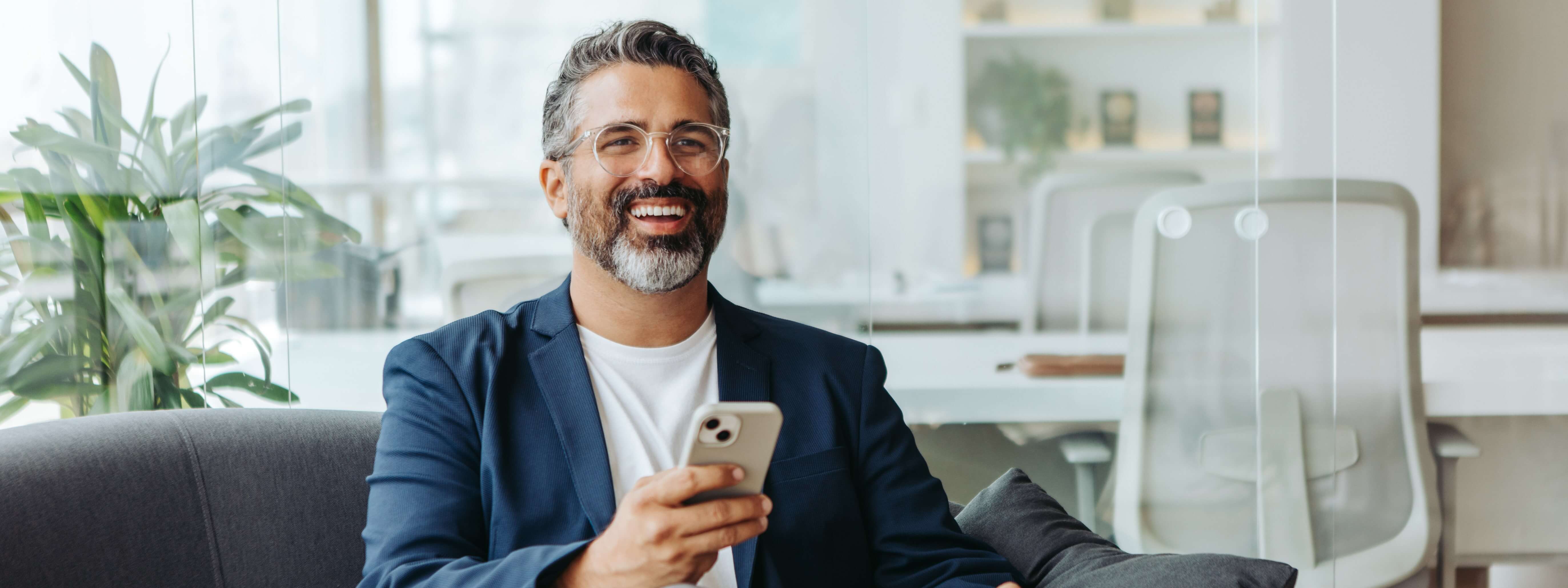 A man smiling holding a phone in a modern office space.